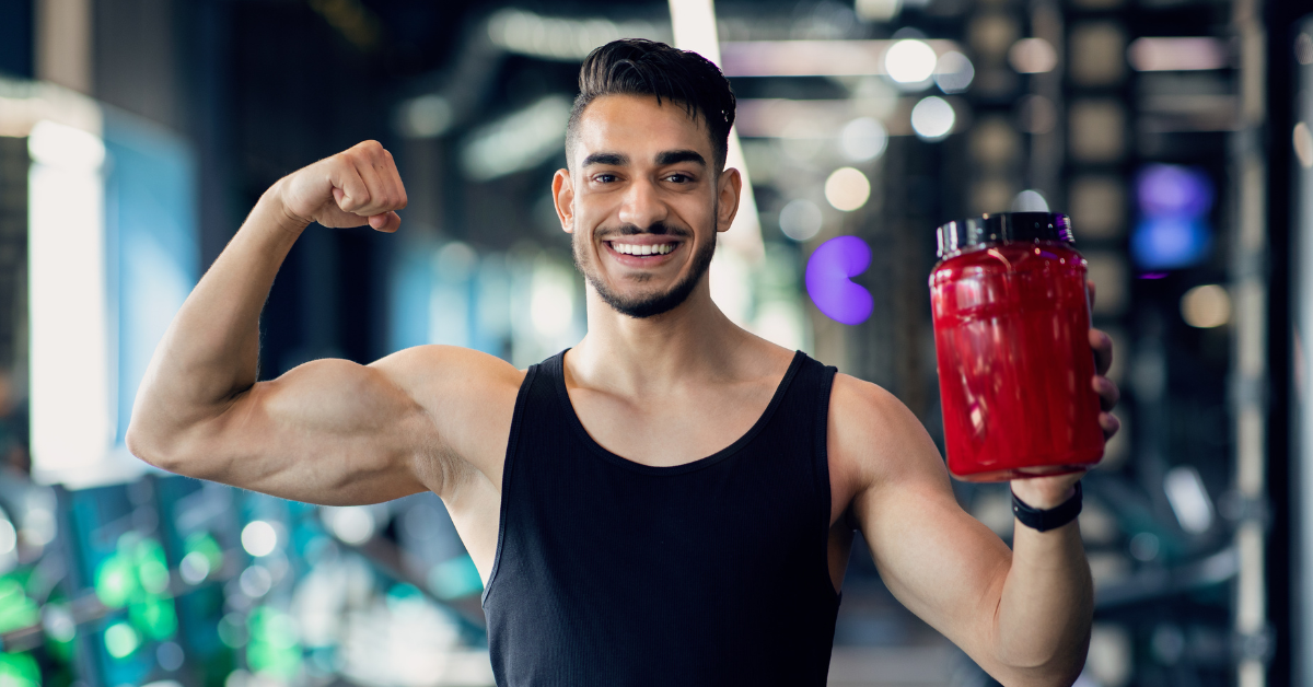 An image showing a person holding a container of creatine supplement with gym equipment in the background.